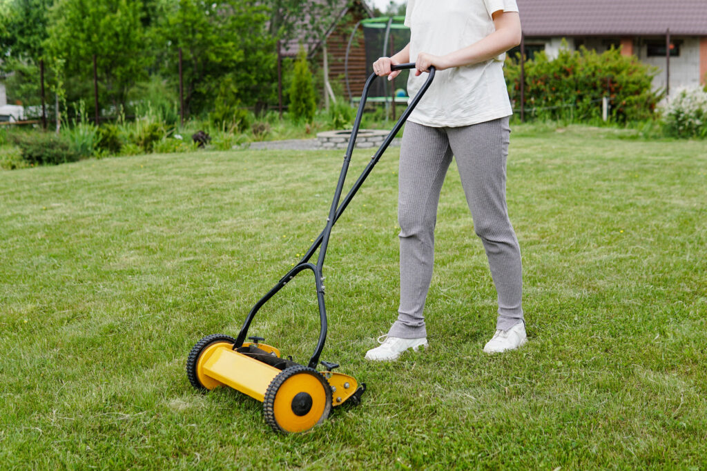 The Ultimate Guide To Grass Cutters: Types, Benefits, And Maintenance 2 Young woman mowing lawn with a manual push lawn mower.