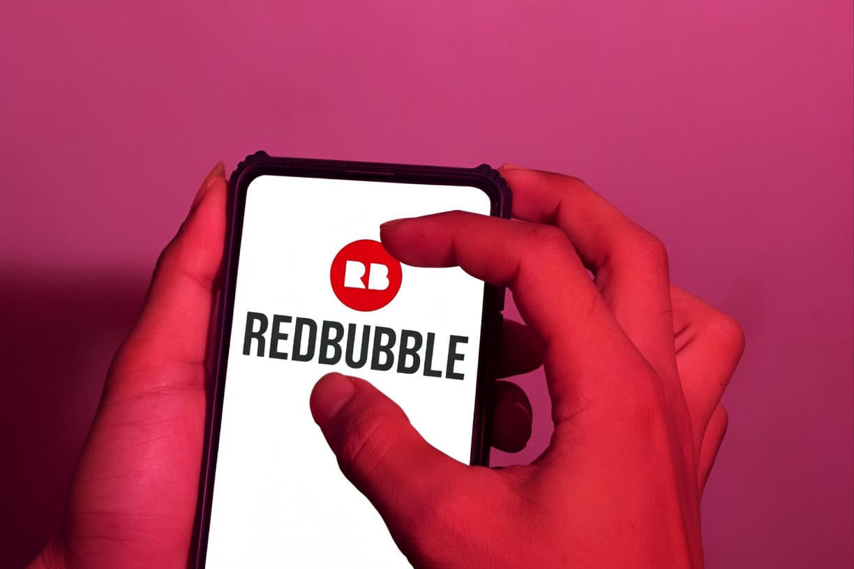 Hands holding a smartphone displaying the Redbubble logo