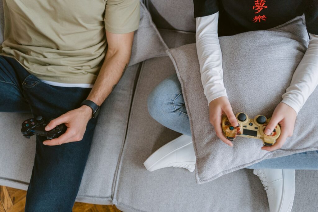 Get Paid to Play Games: 6 Legit Apps to Try 2 A close-up of two individuals enjoying video games with controllers on a sofa.
