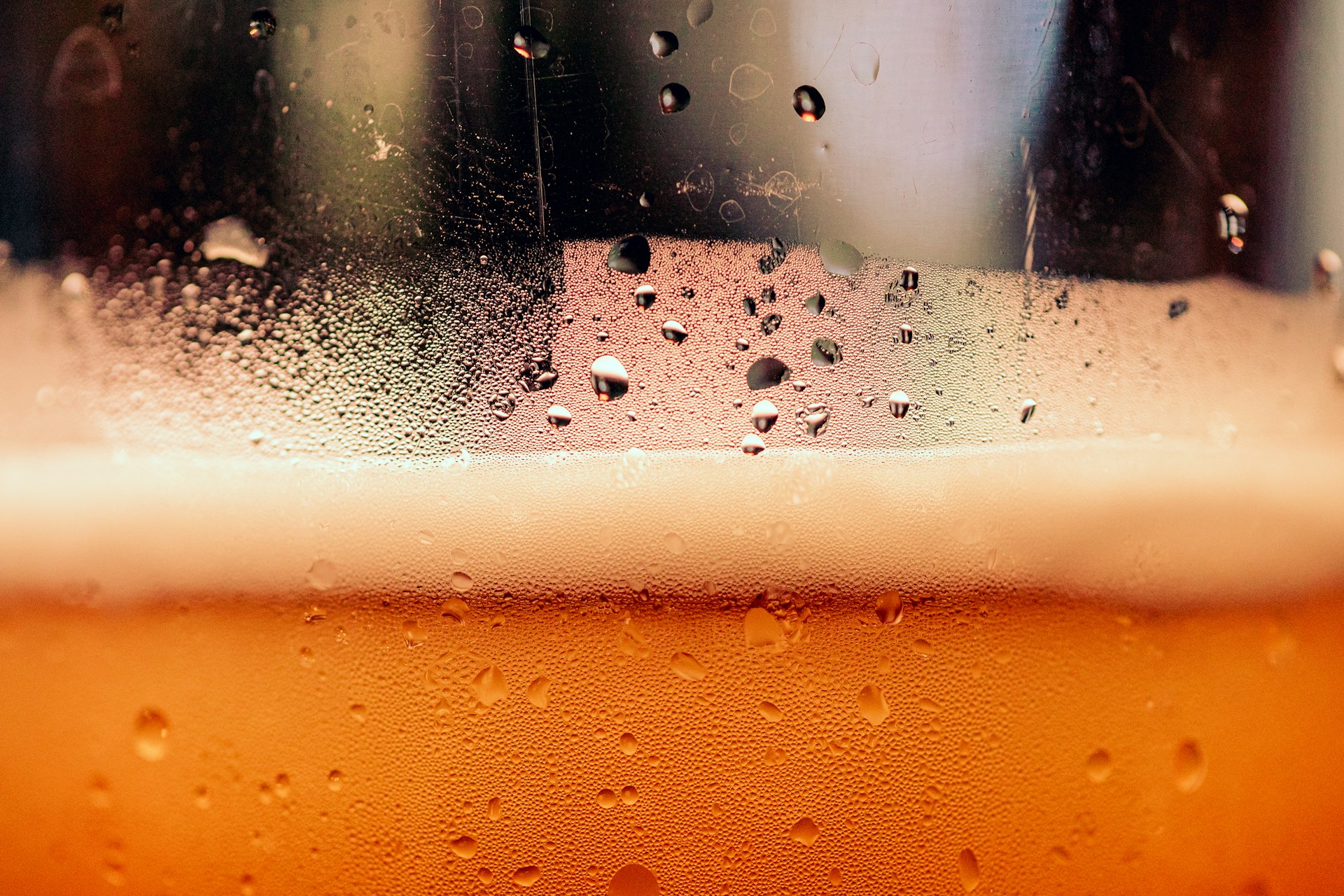 Close-up of condensation droplets on a cold glass filled with amber beer and foam