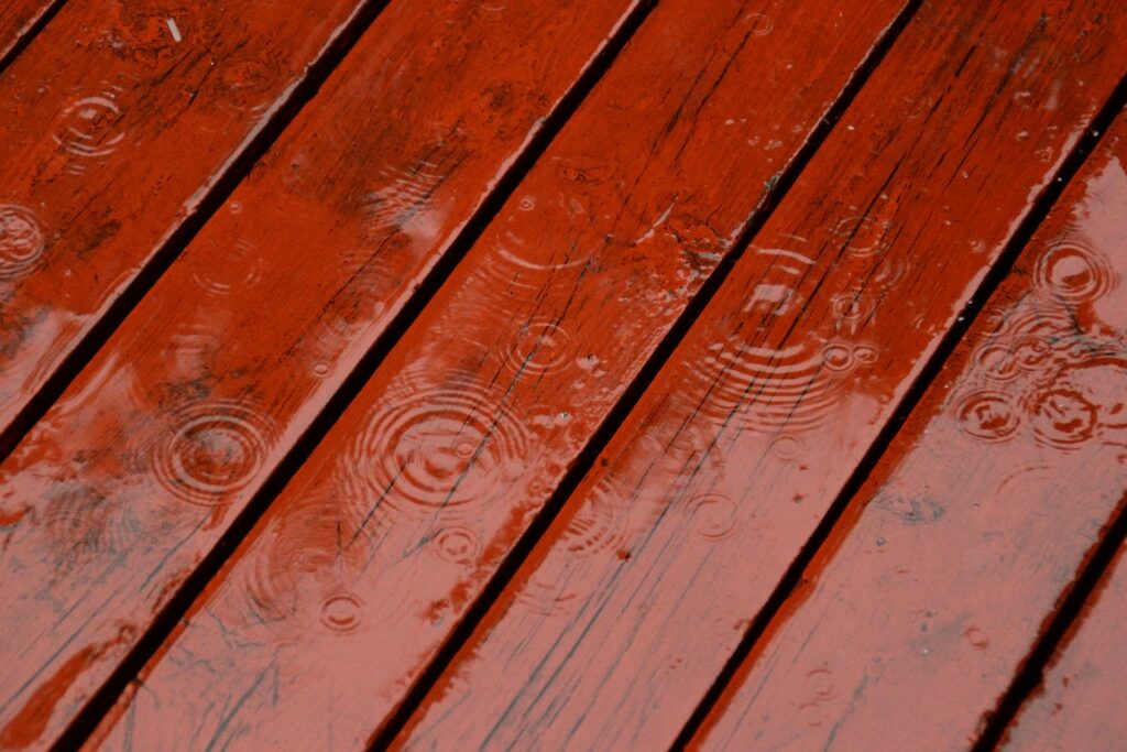 Raindrops creating ripples on wet, reddish-brown wooden deck planks