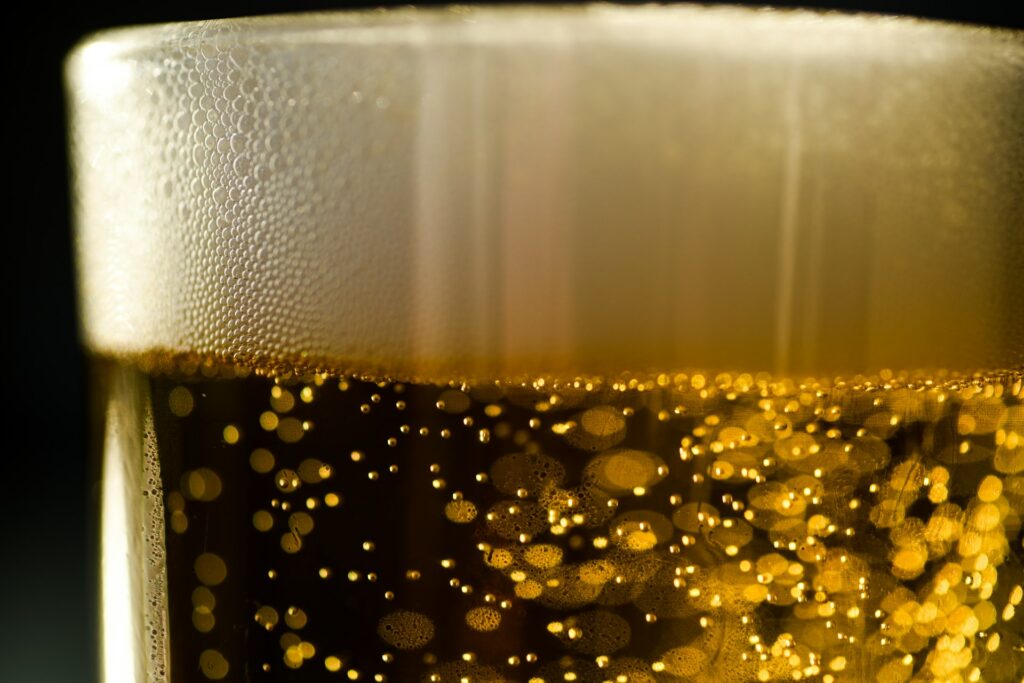 Close-up of golden beer with carbonation bubbles rising to a thick head of foam