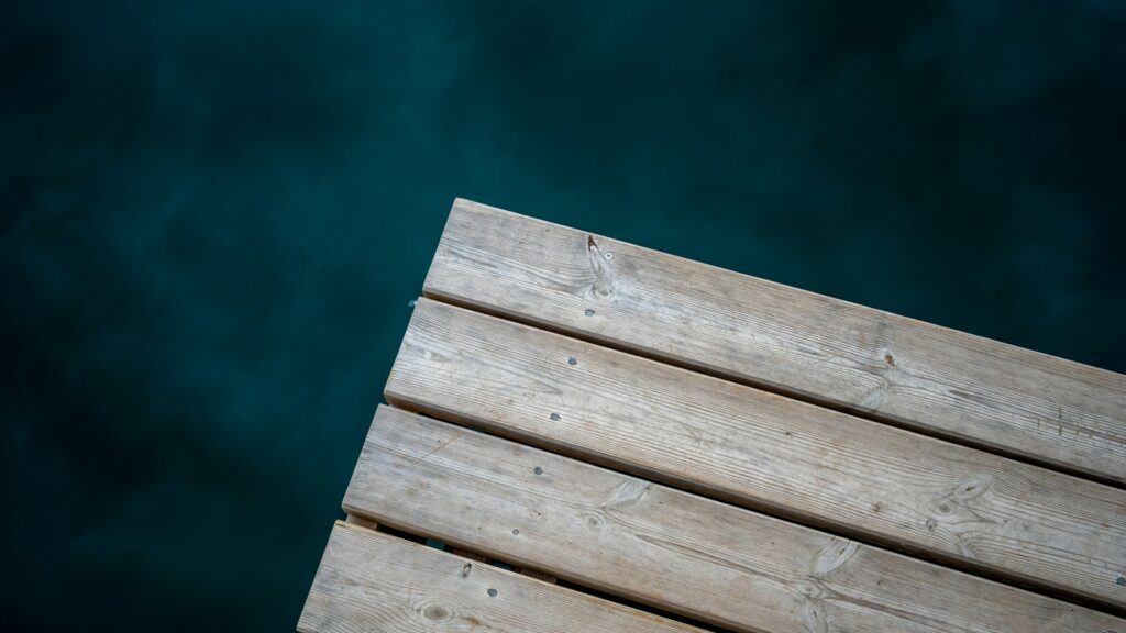 Corner of a light wooden dock extending over deep teal water