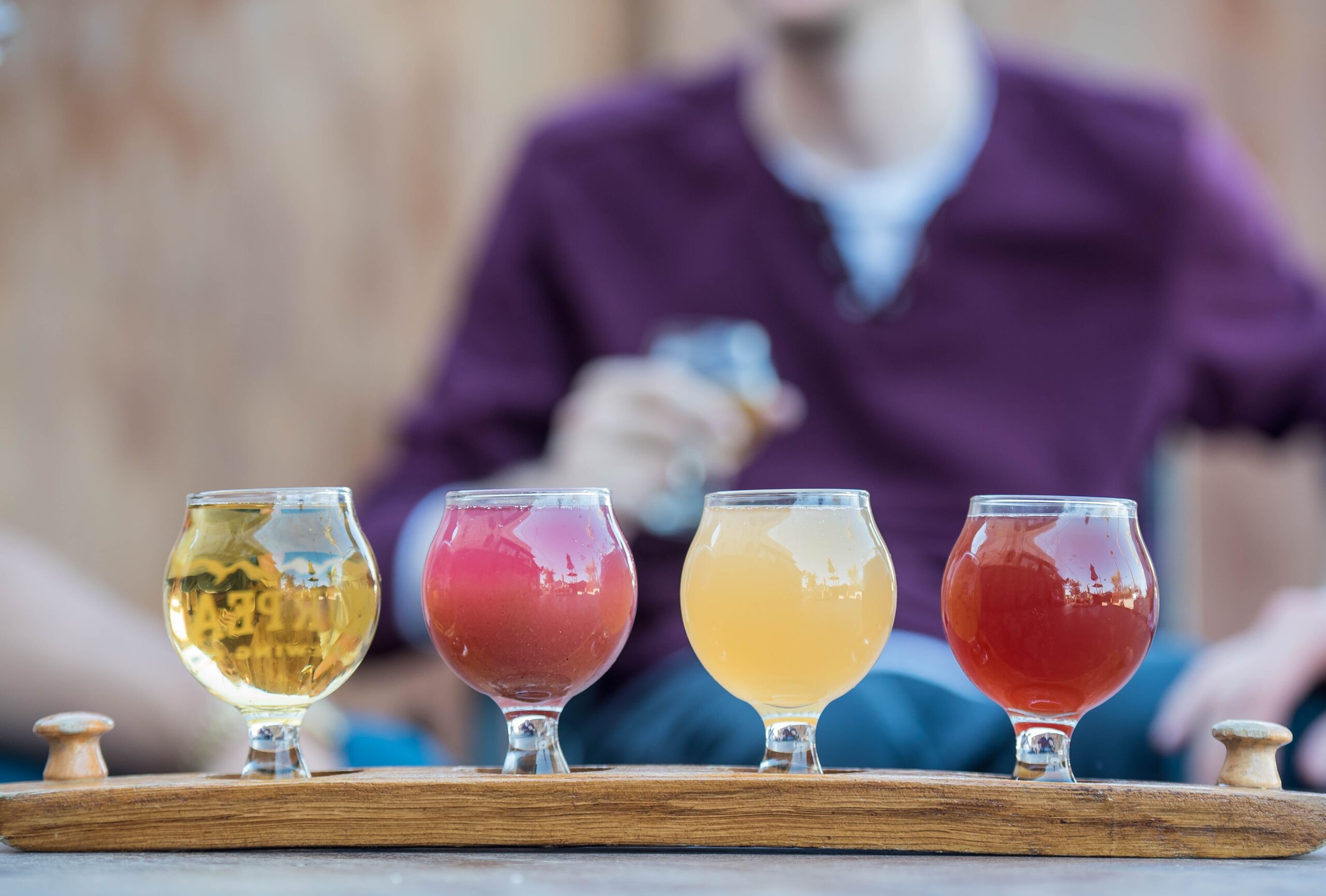 A tasting flight of craft beers displayed on a wooden board with snack pairings
