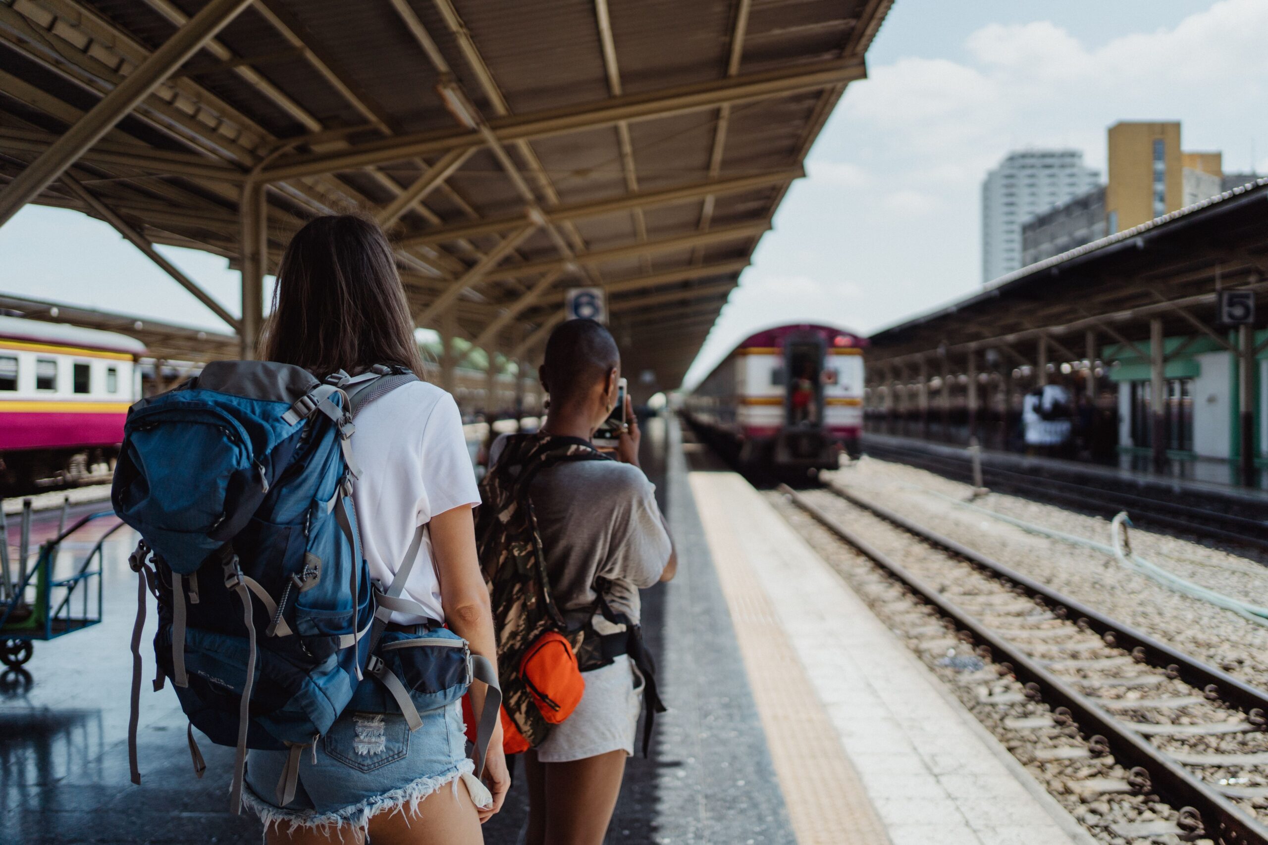 A budget traveler with a backpack checking a map and mobile phone at a sunny train station